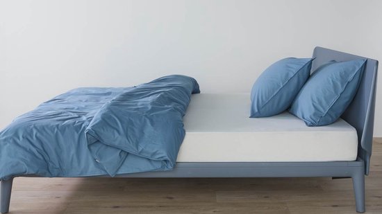 Bed opgemaakt met een blauw dekbed en twee kussens, opgemaakt op een grijs ledikant.