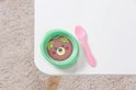 Groen schaaltje met bruine pudding en kiwi, naast een roze lepel op een witte tafel.