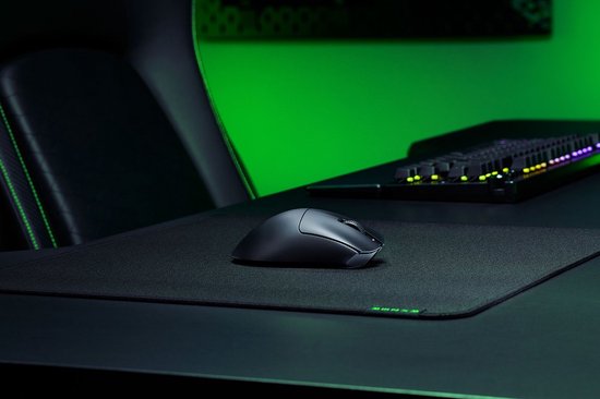 Zwarte Razer DeathAdder V3 hyperspeed gaming muis op een bureau met gaming-uitrusting en groene accentverlichting.