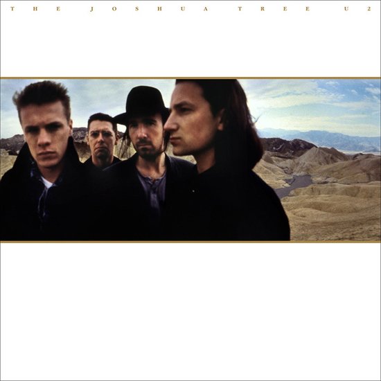 Vier mannen van U2 poseren voor een woestijnlandschap. Tekst bovenaan: The Joshua Tree U2.