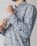 Man die zijn manchet van een blauw overhemd met bladprint aanpast.