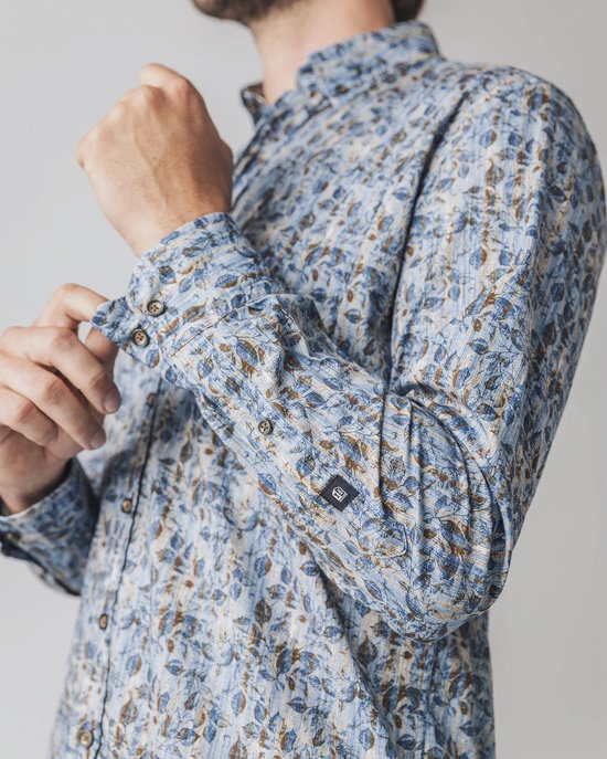 Man die zijn manchet van een blauw overhemd met bladprint aanpast.
