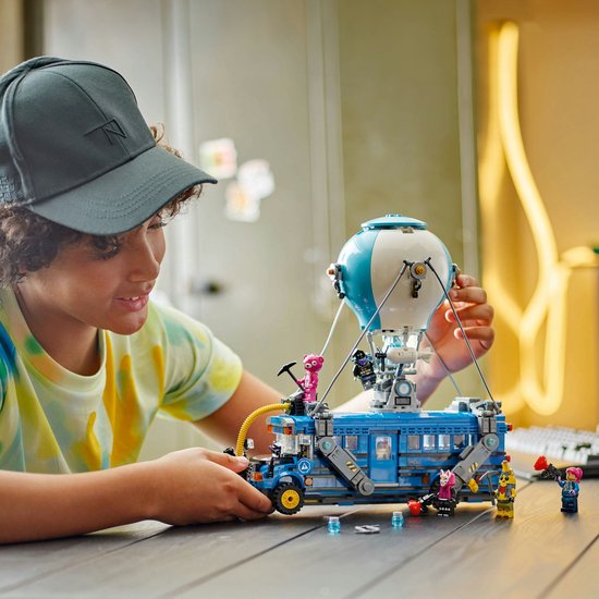 Garçon avec casquette regardant le bus de combat LEGO avec ballon. Figurines sur la table.