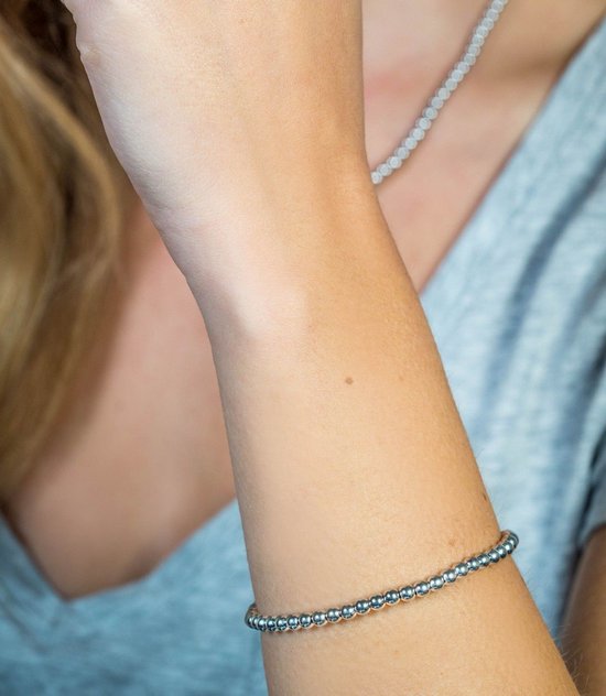 Arm met een zilverkleurige armband van kleine bolletjes, gedragen met een grijs shirt.