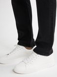 Voeten van een man in zwarte jeans en witte sneakers.