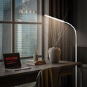 Moderne witte staande lamp naast een bureau met laptop en woondecoratie.