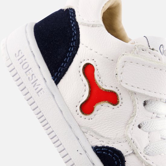 Witte leren sneaker met donkerblauwe suède accenten en een rode X-vormige detail op de zijkant. SHOESME op de zoolrand.