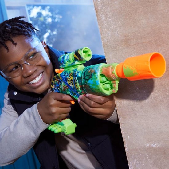 Jongen met veiligheidsbril speelt met groene speelgoedblaster met oranje details, camouflageprint en skull-motief.