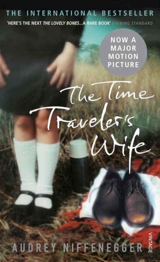 Couverture du livre 'The Time Traveler's Wife', maintenant un film. Une jambe d'enfant avec des bas blancs et des chaussures noires se tient à côté d'une thermos et d'une paire de chaussures sur une couverture.