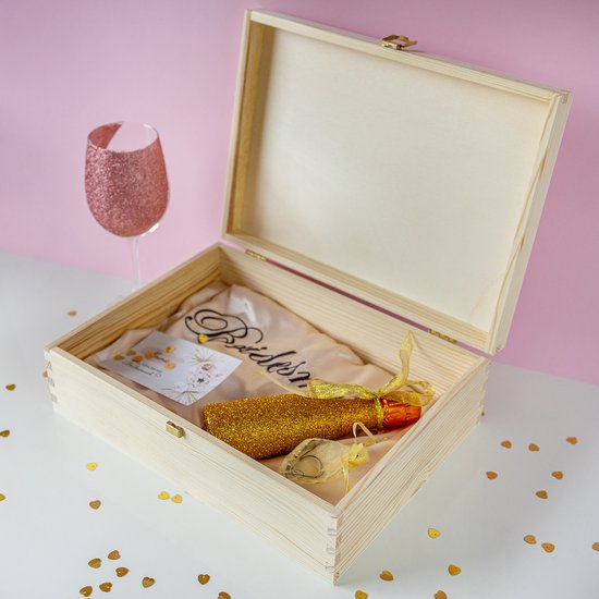 Een open houten kist, met een bruidszijde 'Bridesmaid', een gouden flesje en een glas.