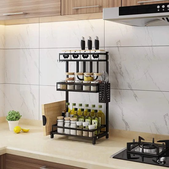 Zwart 3-laags kruidenrek met flessen, potjes, messen en snijplank in een moderne keuken.