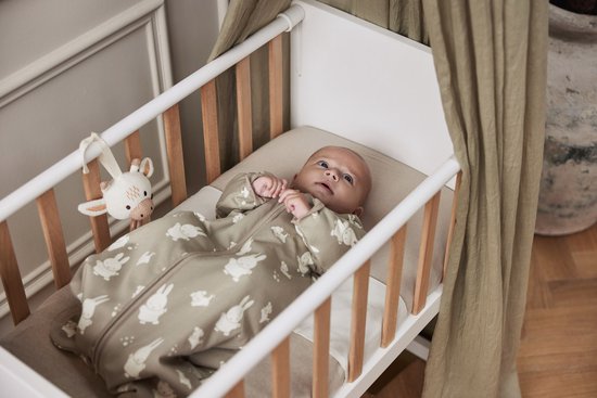 Baby in een olijfgroene slaapzak met Miffy print, liggend in een ledikant.
