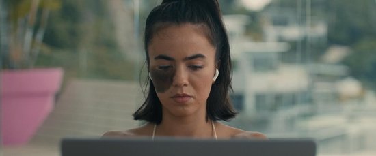 Een jonge vrouw met donker haar, een litteken op haar gezicht en oortjes, kijkt naar een laptop.