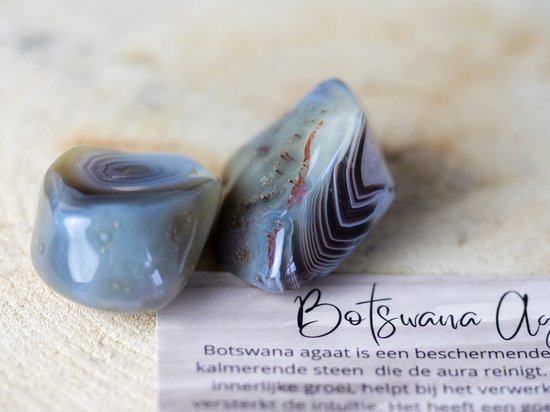 Twee gladde Botswana agaat trommelstenen, grijs, bruin en wit gestreept, met rode accenten.