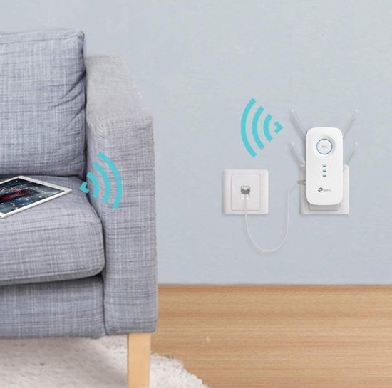 TP-Link RE650 WiFi Range Extender aangesloten in een stopcontact in een woonkamer, nabij een sofa met een tablet.
