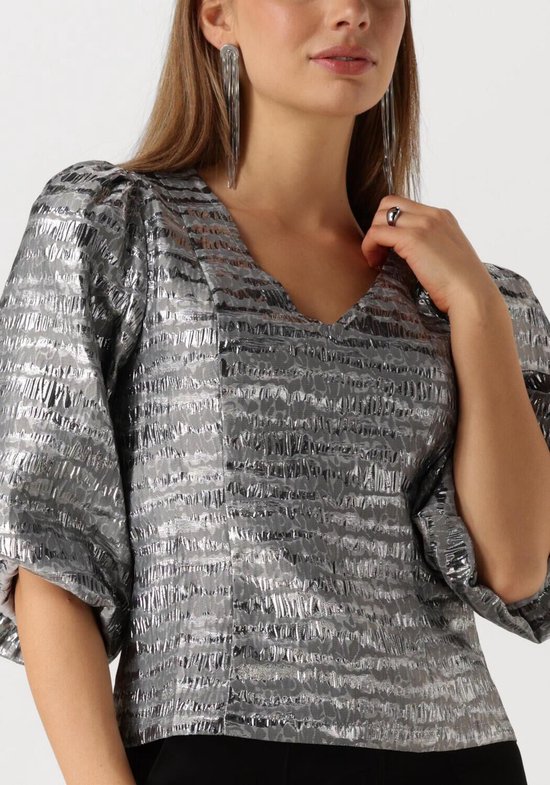 Model draagt zilveren blouse met pofmouwen en V-hals, met horizontale textuur.