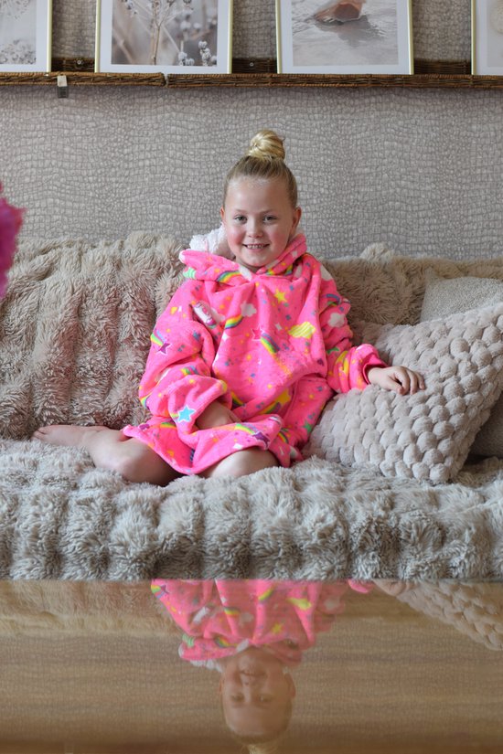 Meisje zittend op een bank in neonroze hoodie deken met eenhoorns, regenboog en sterrenprint.