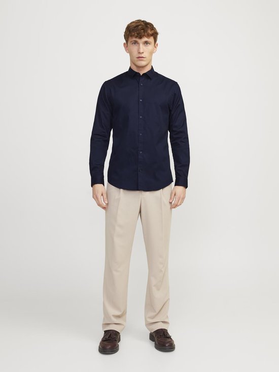 Man met marineblauw overhemd en beige broek, staand, voorkant.