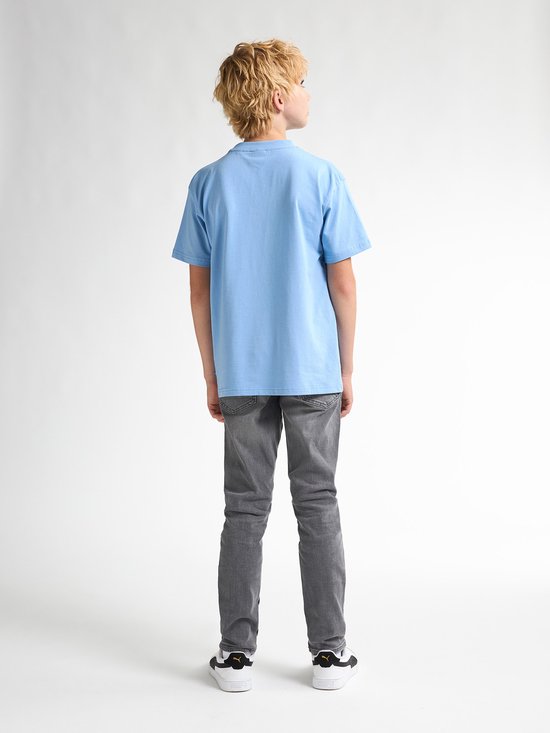 Jongen in lichtblauwe T-shirt en grijze jeans, van achteren gezien.