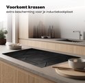 Zwarte inductiebeschermer met geometrisch tegelpatroon op een inductiekookplaat in een keuken.