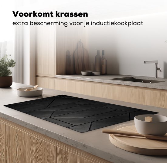 Zwarte inductiebeschermer met geometrisch tegelpatroon op een inductiekookplaat in een keuken.