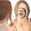 Een vrouw brengt make-up aan, gefocust op haar wenkbrauw via een vergrootglas.