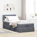 Donkergrijs bed met gestoffeerd hoofdbord, opbergruimte en witte matrastopper.