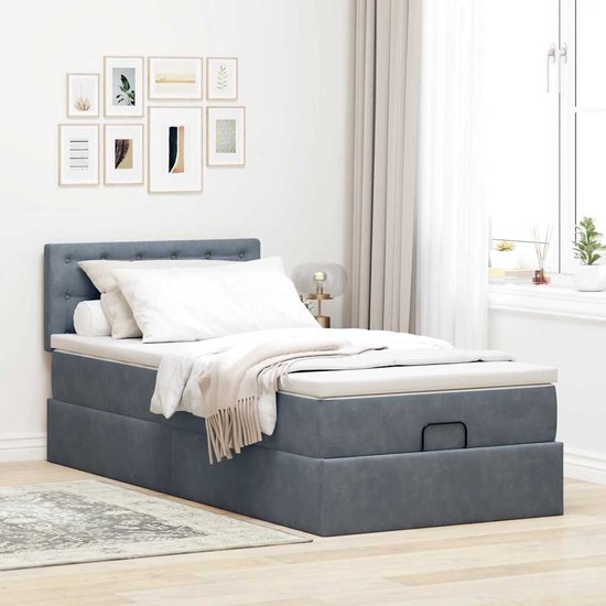 Donkergrijs bed met gestoffeerd hoofdbord, opbergruimte en witte matrastopper.
