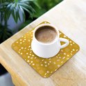 Sous-verre doré à motif de Noël blanc avec une tasse de café dessus.