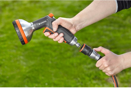 Hand koppelt GARDENA spuitpistool aan een zwarte en oranje tuinslang.