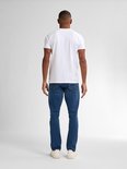 Man staat van achteren in een witte t-shirt en een blauwe spijkerbroek met rechte pasvorm, met witte sneakers.