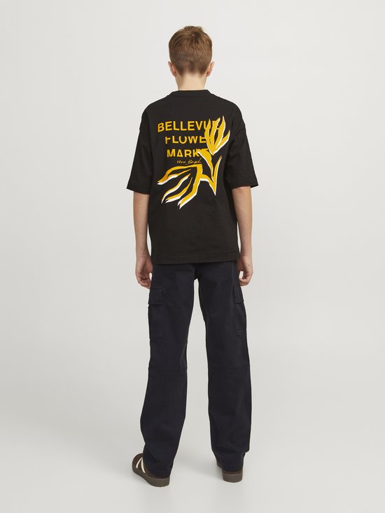 Jongen met rug naar de camera, draagt zwart T-shirt met gele print en donkerblauwe cargo broek.