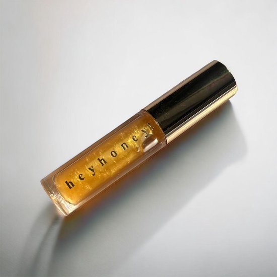 Gouden lipgloss met "hey honey!" op de tube, op een witte achtergrond.
