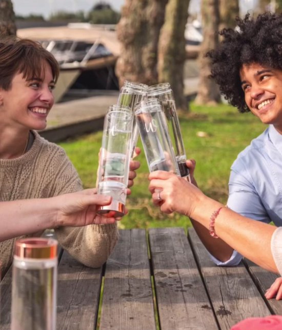 Vier mensen proosten met glazen waterflessen met koperkleurige dop en rozenkwarts kristallen.