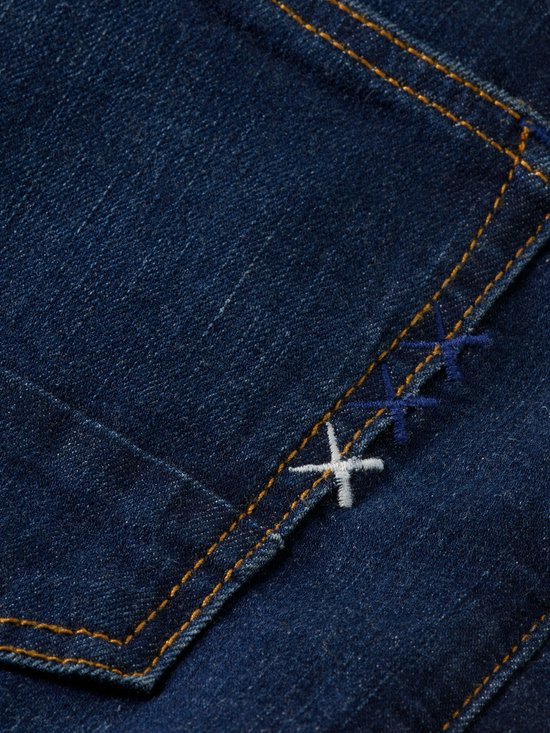 Detail van donkerblauwe jeansstof met gele en blauwe kruisstiksels op de zak.