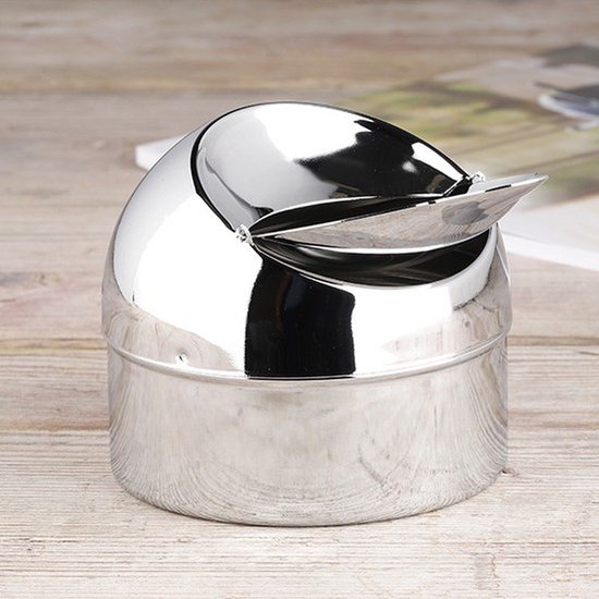 Zilverkleurige metalen asbak met klep, op houten ondergrond.