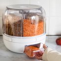 Een hand trekt een lade uit een witte voorraaddispenser met vier vakken, gevuld met linzen.