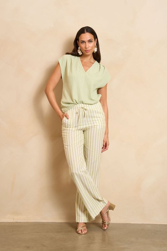 Model draagt een mintgroene top met V-hals en een bijpassende gestreepte broek. Goudkleurige sandalen en opvallende oorbellen.