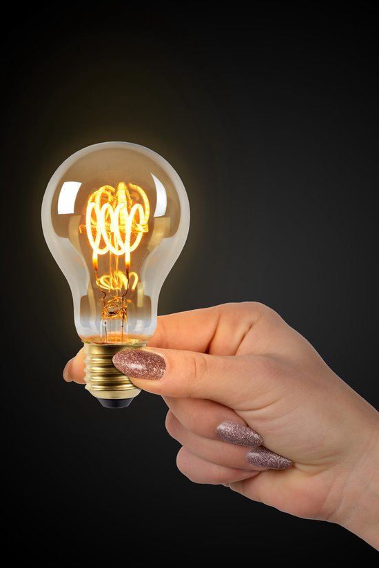 Une main avec des ongles pailletés tient une ampoule LED E27 ambrée incandescente avec un filament en spirale.