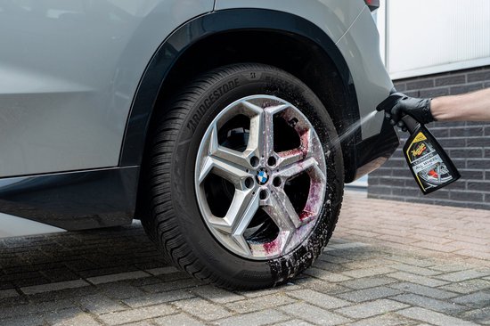 Hand met handschoen spuit velgenreiniger op een zilveren BMW velg. De reiniger kleurt rood.