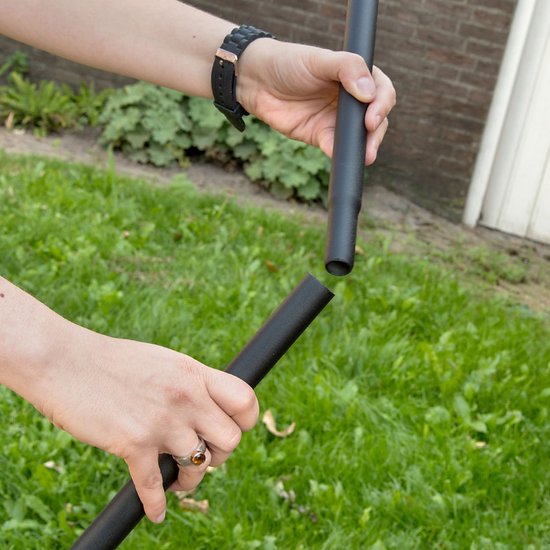 Handen die twee zwarte metalen stokdelen met elkaar verbinden boven een grasveld.