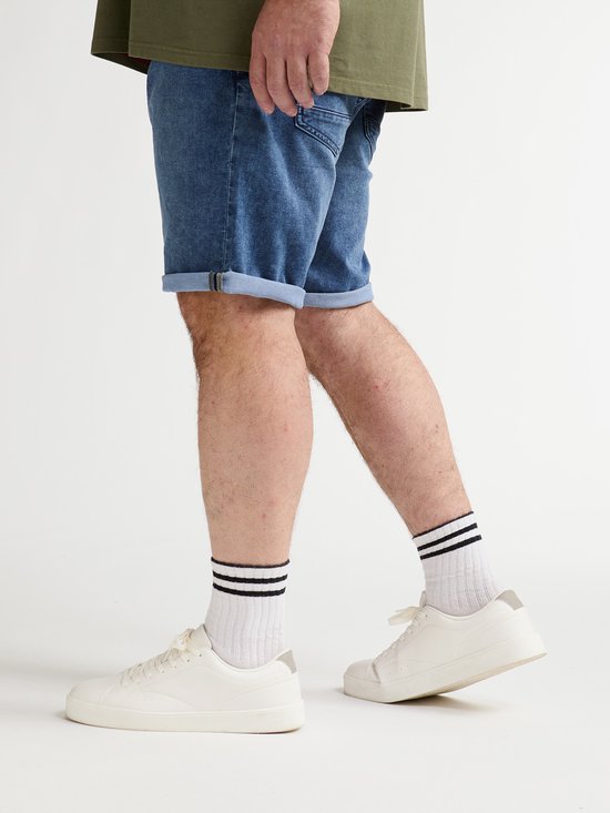 Blauwe jeansshort met omgeslagen zomen, gedragen met witte sneakers en sokken met twee zwarte strepen.
