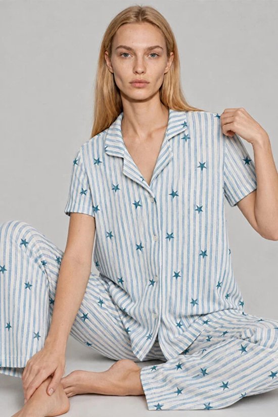 Zittend model met gestreepte pyjama met korte mouwen en sterrenprint in lichtblauw en wit.