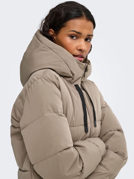 Zijaanzicht van een model in een beige pufferjas, armen over elkaar, met focus op de kraag.