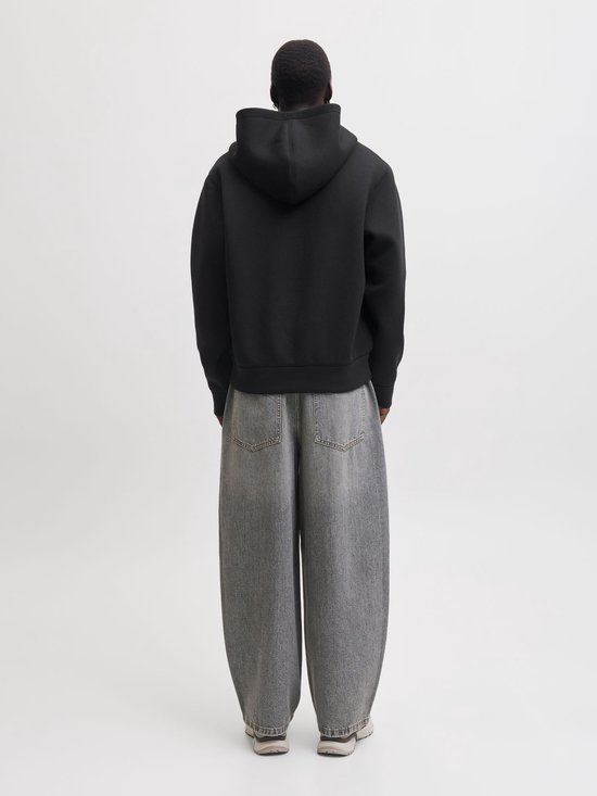 Achteraanzicht van een zwart scuba-vest met capuchon en grijze wijde jeans.