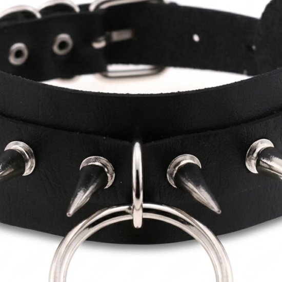 Close-up van een zwarte choker met metalen spikes en een grote ring.