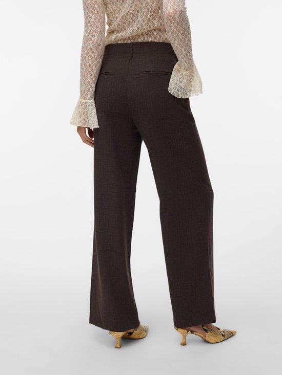 Model van achteren gezien, draagt een donkerbruine broek met wijde pijpen en een pinstreep. Draagt ook een beige kanten blouse.