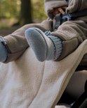 Baby met blauwe gebreide slofjes met veters, zittend in een kinderwagen.