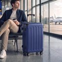 Man met een donkerblauwe koffer op wielen in een luchthaven lounge.