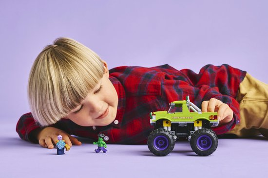 Jongen kijkt naar LEGO monster truck, Hulk en paarse minifiguur.